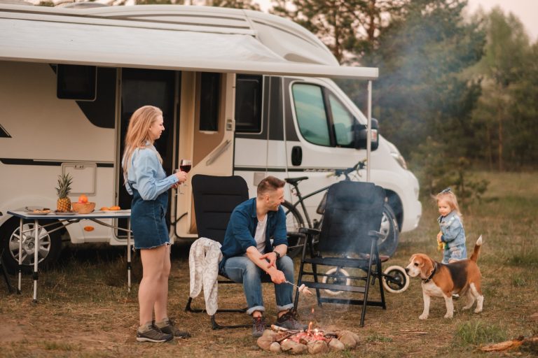 A family cooks sausages on a bonfire near their motorhome in the woods